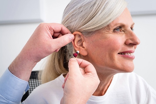 Ältere Frau bekommt ein modernes Hörgerät ins Ohr eingesetzt, Hörgeräte Anpassung.